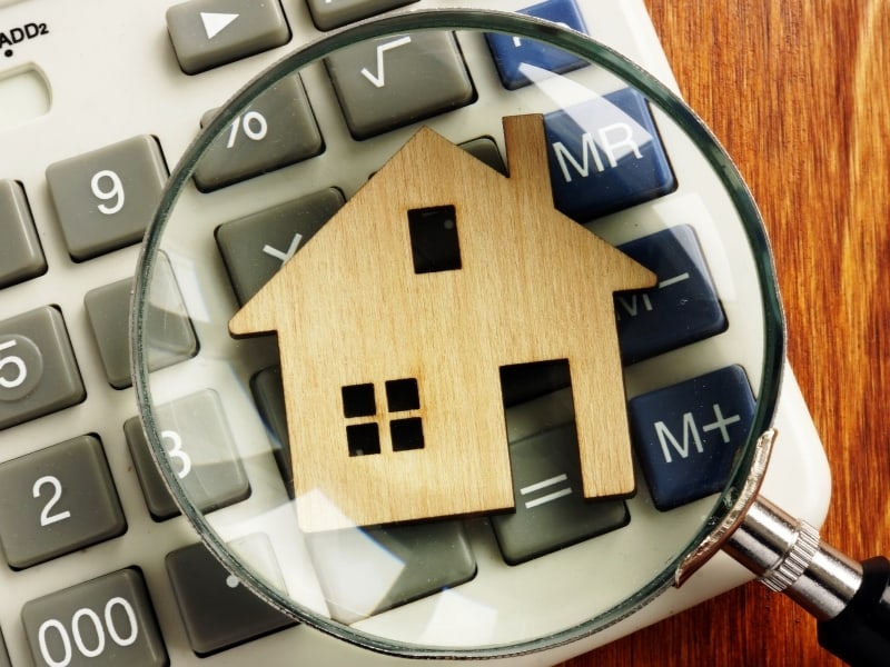 A wooden home under a magnifying glass on top of a calculator